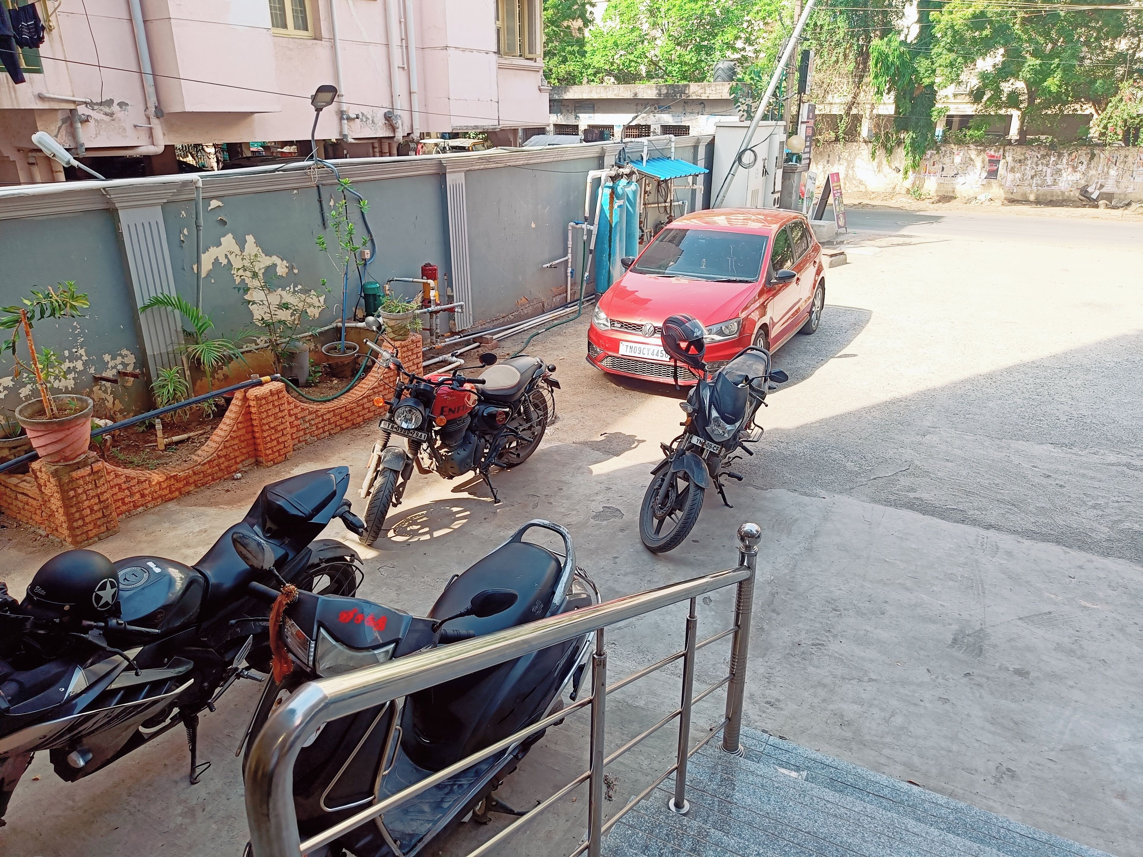 A parking area with motorcycles and a red car.