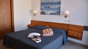 A neatly made bed with a striped bedspread, a handbag, and a book on it. There is a painting of a sailboat on the wall above the bed. - La Gioiosa (Finale Ligure)