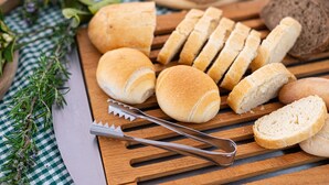 Various types of bread on a wooden cutting board with a knife and bread slicer. - La Gioiosa (Finale Ligure)