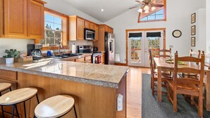 A modern kitchen with granite countertops, wooden cabinets, and a dining area with a wooden table and chairs. - Broken Arrow Abode (Overgaard)