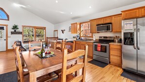 A spacious kitchen with wooden cabinets, a stainless steel refrigerator, and a dining area with a wooden table and chairs. - Broken Arrow Abode (Overgaard)