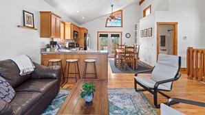 A spacious living area with a leather sofa, a coffee table with a plant, and a bar area with stools. - Broken Arrow Abode (Overgaard)