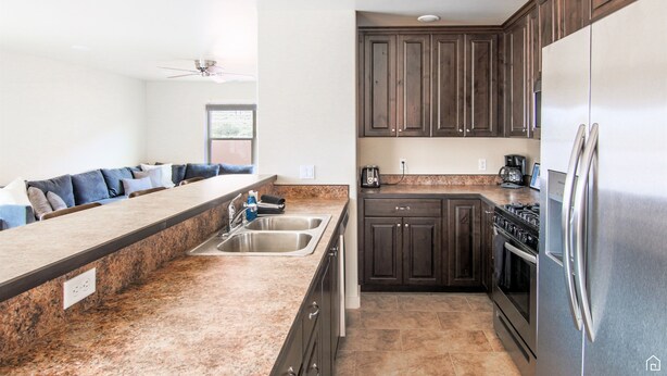 A modern kitchen with granite countertops, dark wooden cabinets, stainless steel appliances, and a built-in oven. - Moab Mirage Hot Tub and Pool (Moab)