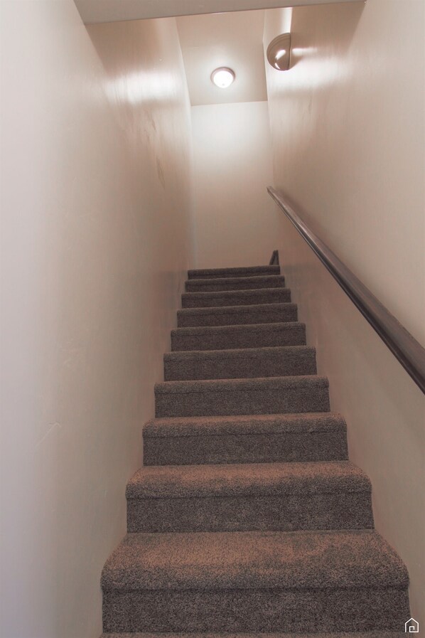 A staircase with carpeted steps and a handrail, leading to a landing with a light fixture.