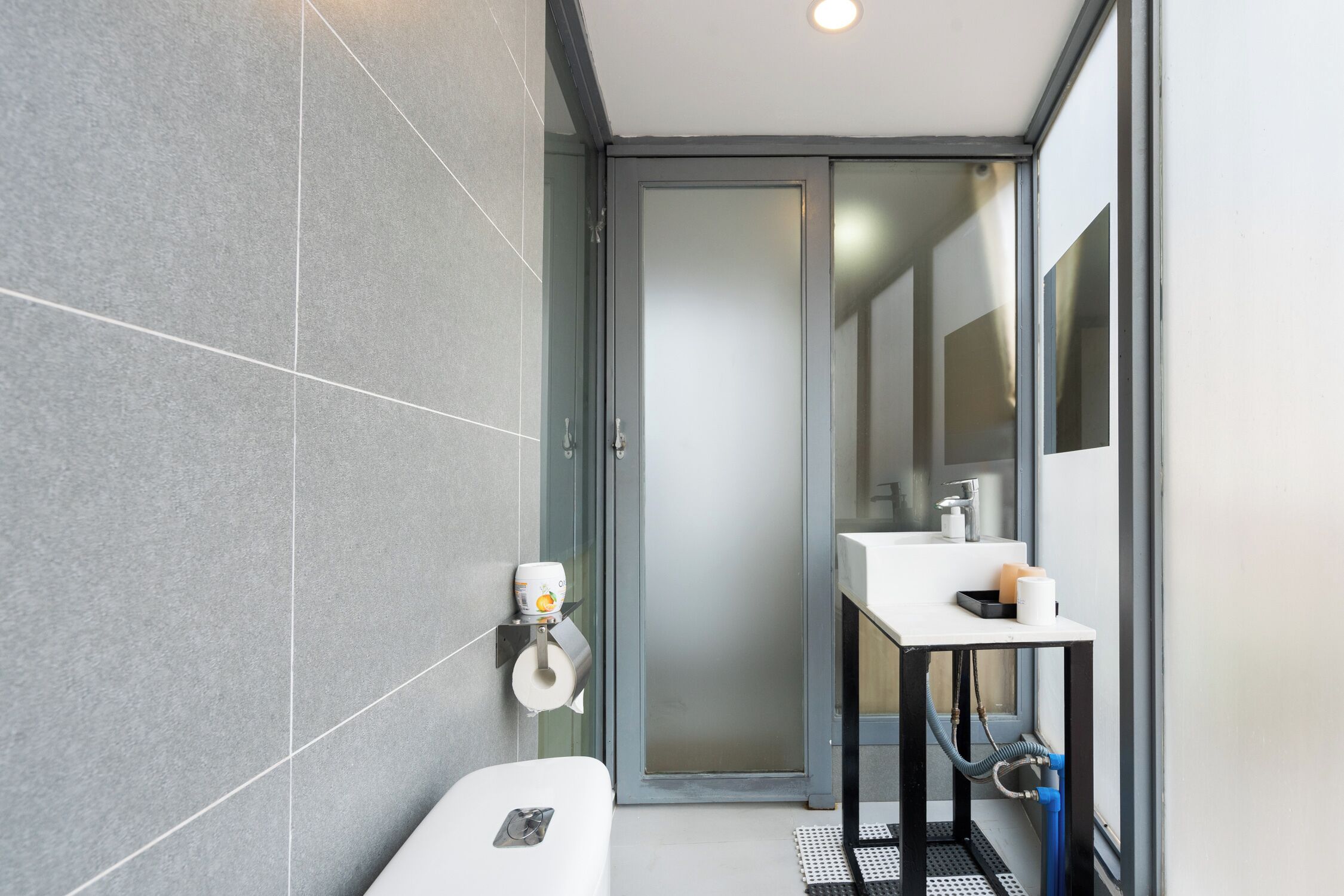 Une salle de bain moderne équipée de toilettes, d’un lavabo et d’une porte en verre donnant accès à l’espace de la douche.