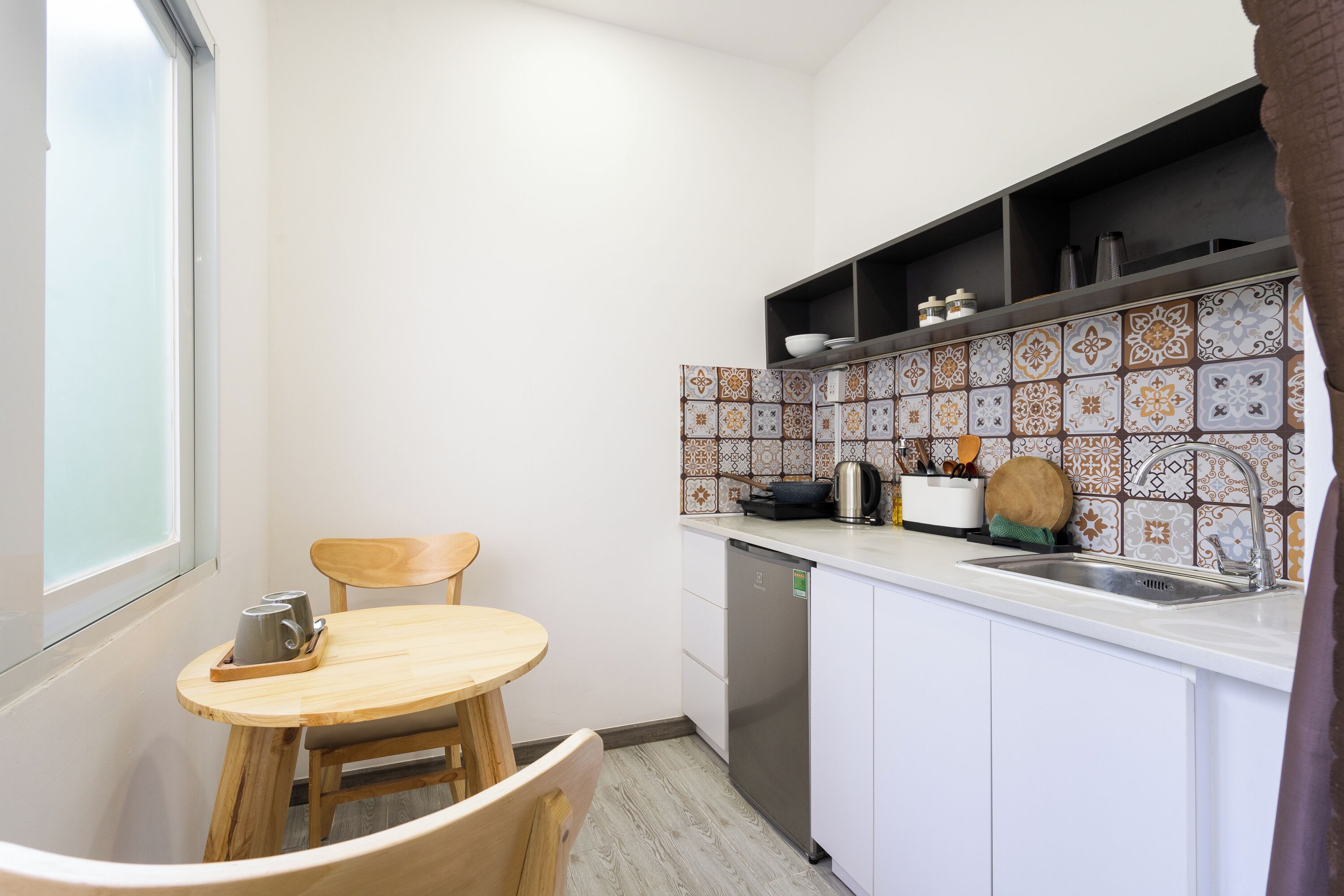 A compact kitchen with a wooden table and chairs, a built-in dishwasher, and a tiled backsplash.
