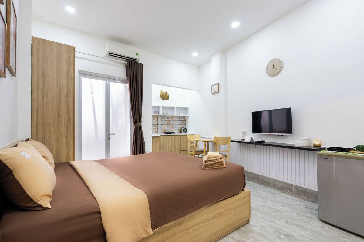 Ein modernes Hotelzimmer mit einem Holzbett, einem Fernseher, einer Küchenzeile und einem Badezimmer.