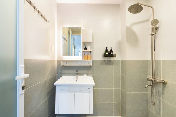 A bathroom with a white sink, a mirror, a shower, and a towel rack.