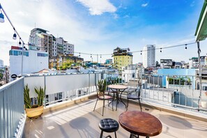 A rooftop terrace with a table and chairs, potted plants, and a view of the cityscape.
