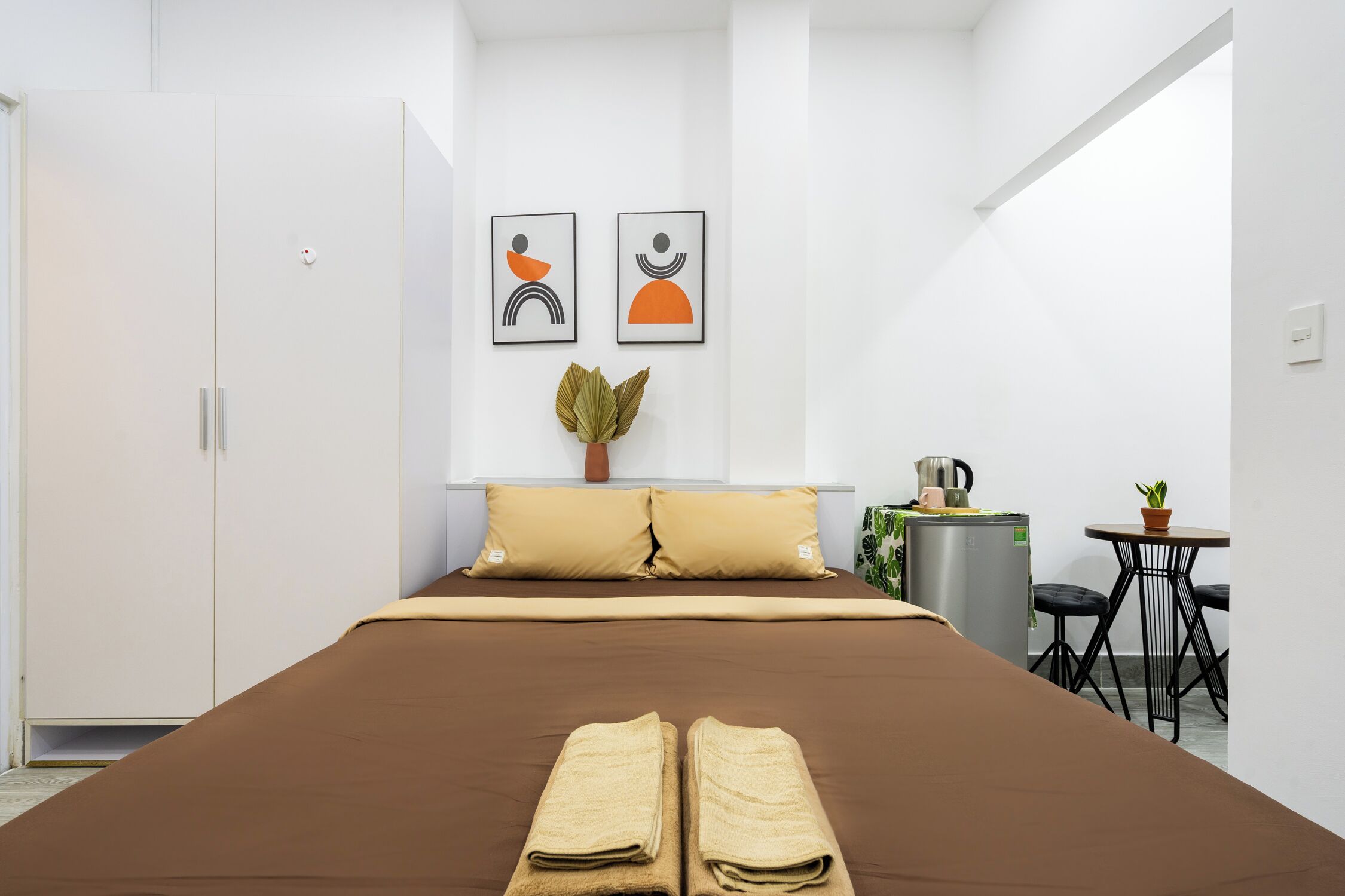 Une chambre d’hôtel moderne avec un grand lit, une petite table agrémentée d’une plante et un coin cuisine.