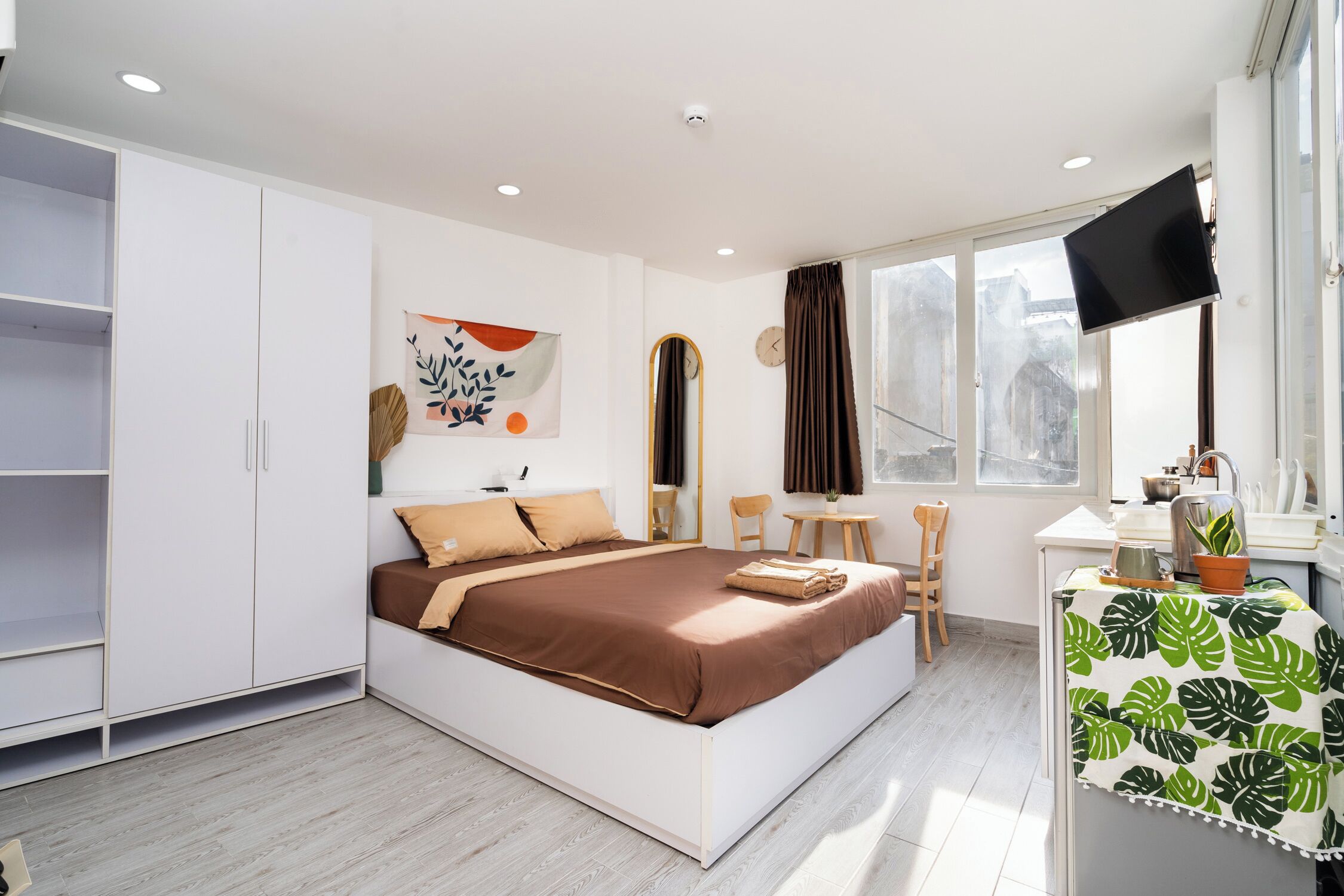 Une chambre moderne avec un grand lit, une armoire, un bureau avec une télévision et une fenêtre avec des rideaux.
