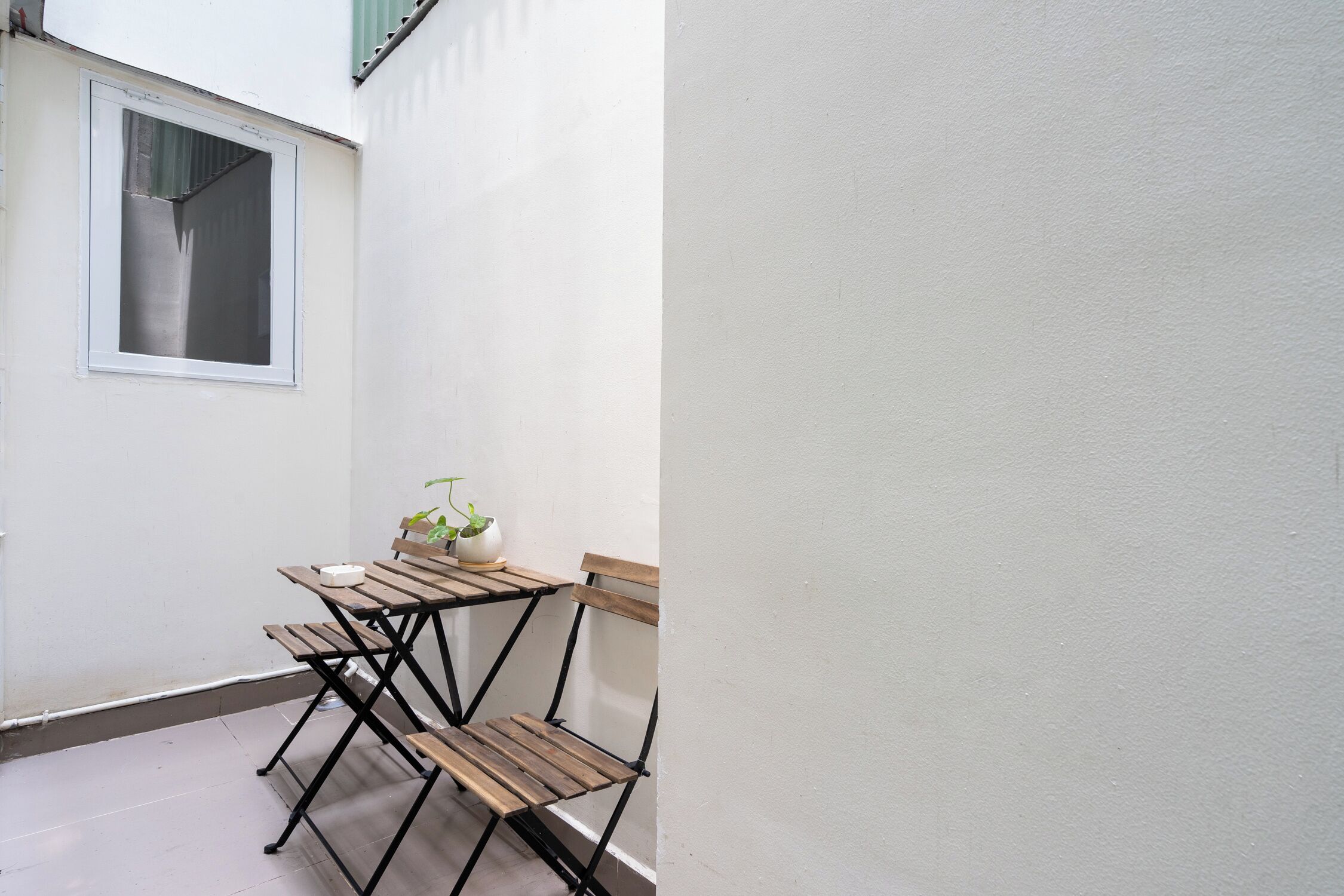 A small outdoor seating area with a table and two chairs, a potted plant, and a window.