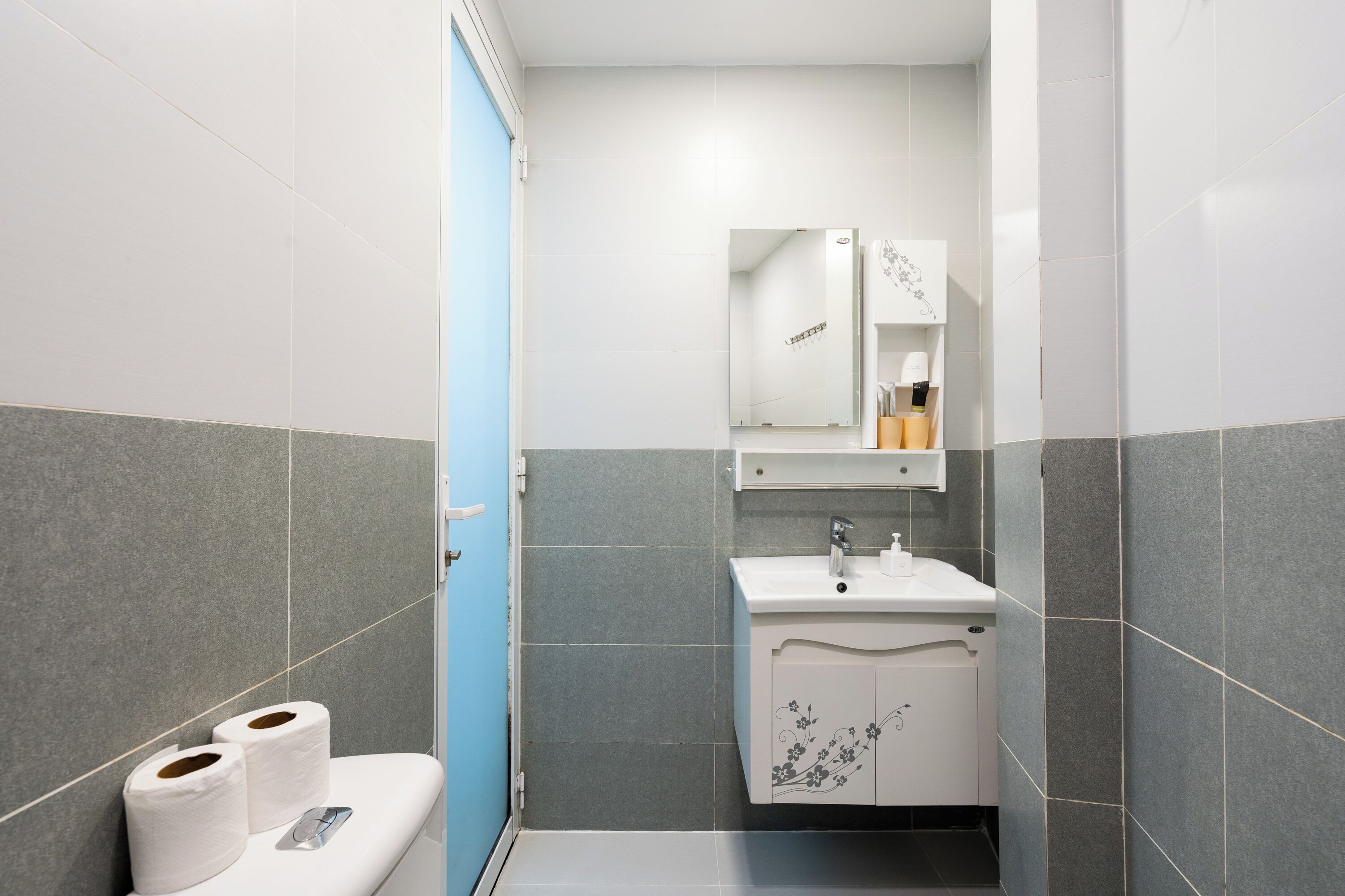A bathroom with a toilet, two rolls of toilet paper, a sink, and a mirror above it.