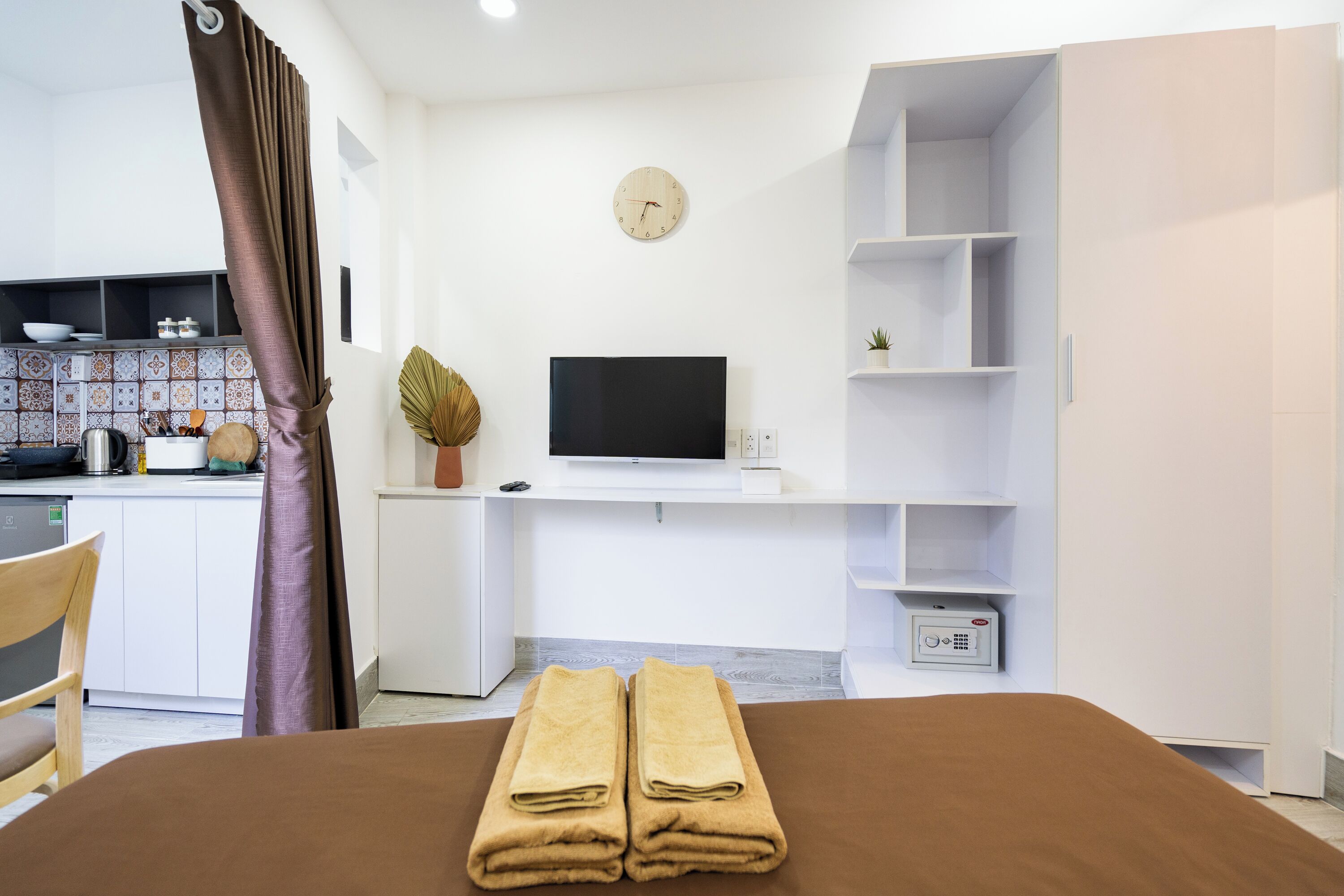 A modern hotel room with a bed, a flat-screen TV, a clock, and a small plant.