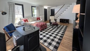 A living room with a sofa, a checkered rug, a black stove, and a staircase. - Litchfield Modern Farmhouse (Litchfield)