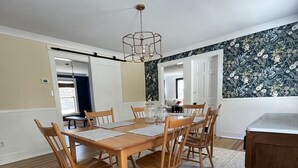 A dining area with a wooden table and chairs, a hanging light fixture, and a patterned wall. - Litchfield Modern Farmhouse (Litchfield)