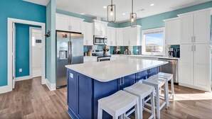 A kitchen with a central island, white cabinets, a stainless steel refrigerator, and a microwave. - Oceanview Dog Friendly Home with Heated Pool and Golf Cart, 7 Green Pelicans (Oak Island)