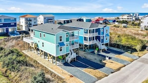 A coastal house with multiple levels, elevated on stilts, featuring a spacious outdoor area with a view of the beach and ocean. - Oceanview Dog Friendly Home with Heated Pool and Golf Cart, 7 Green Pelicans (Oak Island)