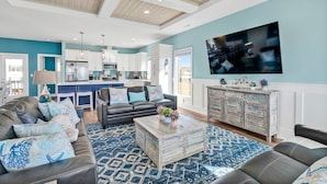A modern living room with a sofa, coffee table, and a TV mounted on the wall. - Oceanview Dog Friendly Home with Heated Pool and Golf Cart, 7 Green Pelicans (Oak Island)