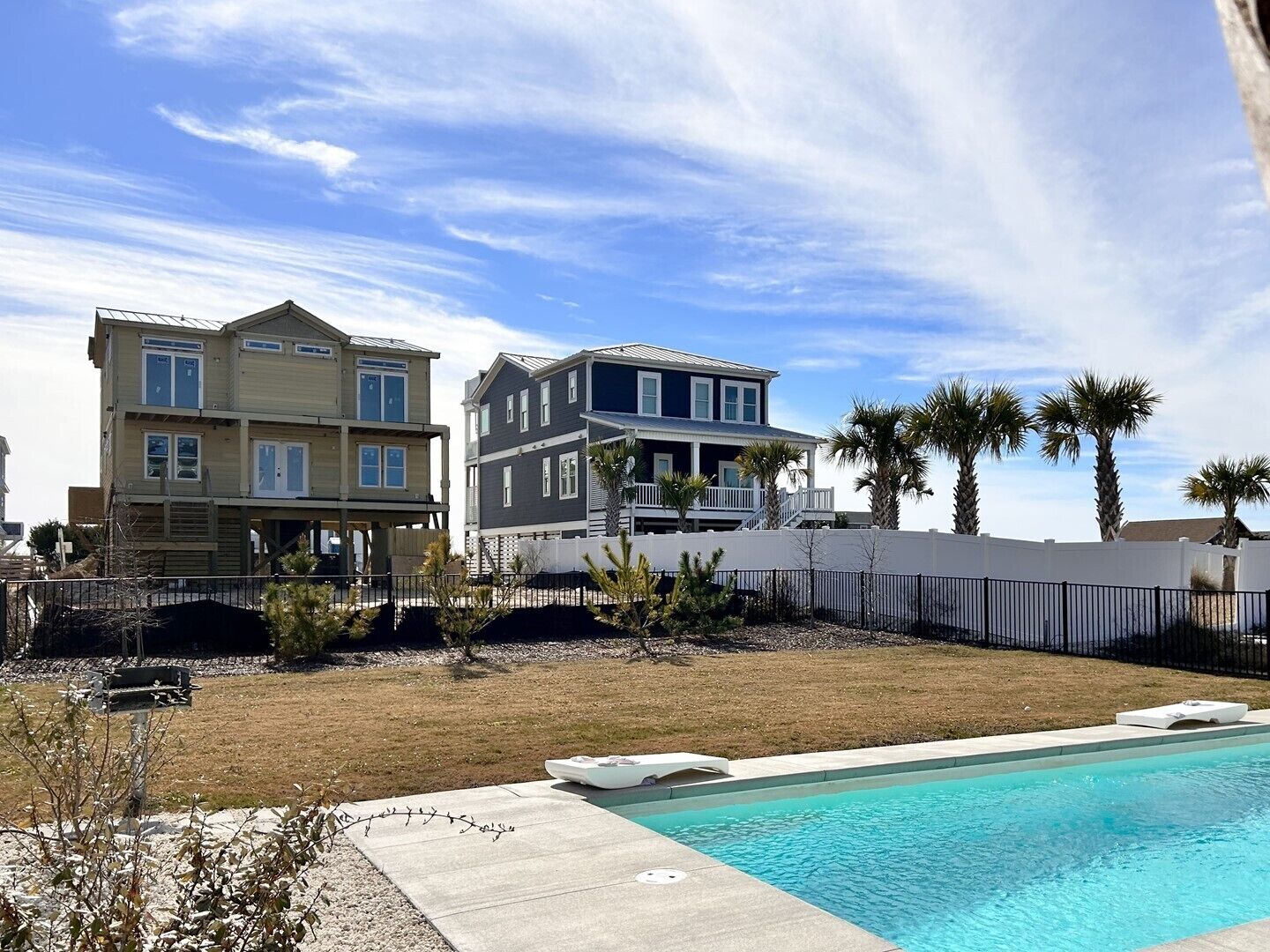 A two-story house with a pool, surrounded by a white fence and palm trees.