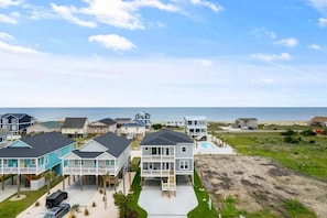 A coastal residential area with houses, a swimming pool, and a beach in the background.