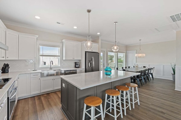 A modern kitchen with white cabinetry, a large island with stools, stainless steel appliances, and pendant lighting.