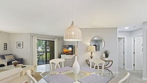 A modern dining area with a glass table, white chairs, and a hanging light fixture.