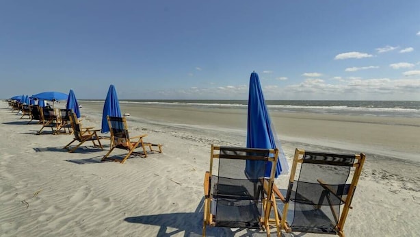 A beach with rows of wooden beach chairs and blue umbrellas.