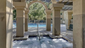 A hot tub area with a canopy, pool, and lounge chairs.