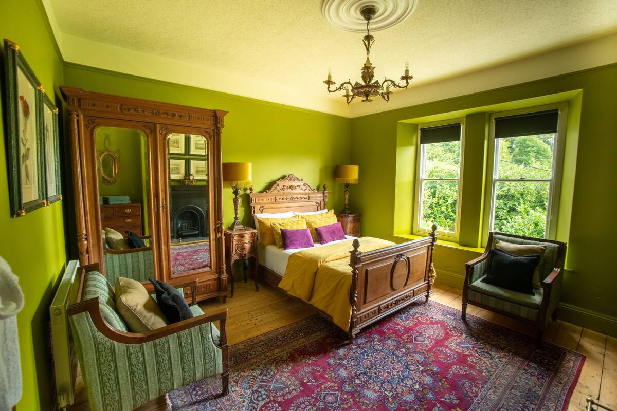 A room with a bed, a chair, a mirror, and a window.