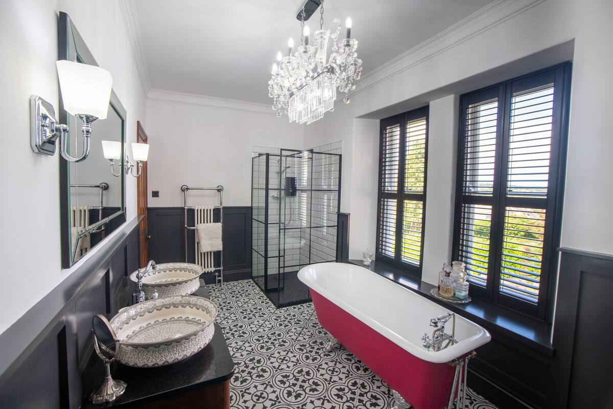 A bathroom with a freestanding bathtub, two sinks, a glass shower enclosure, and a chandelier.