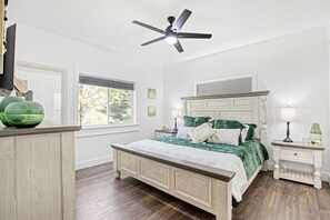A bedroom with a large bed, a ceiling fan, a window, and a nightstand with a lamp. - Amazing Sunset Lake Views, Huge Deck & Hot Tub! (Sunrise Beach)