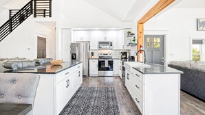 Une cuisine moderne avec des meubles blancs, un îlot central et un escalier menant à un niveau supérieur.
