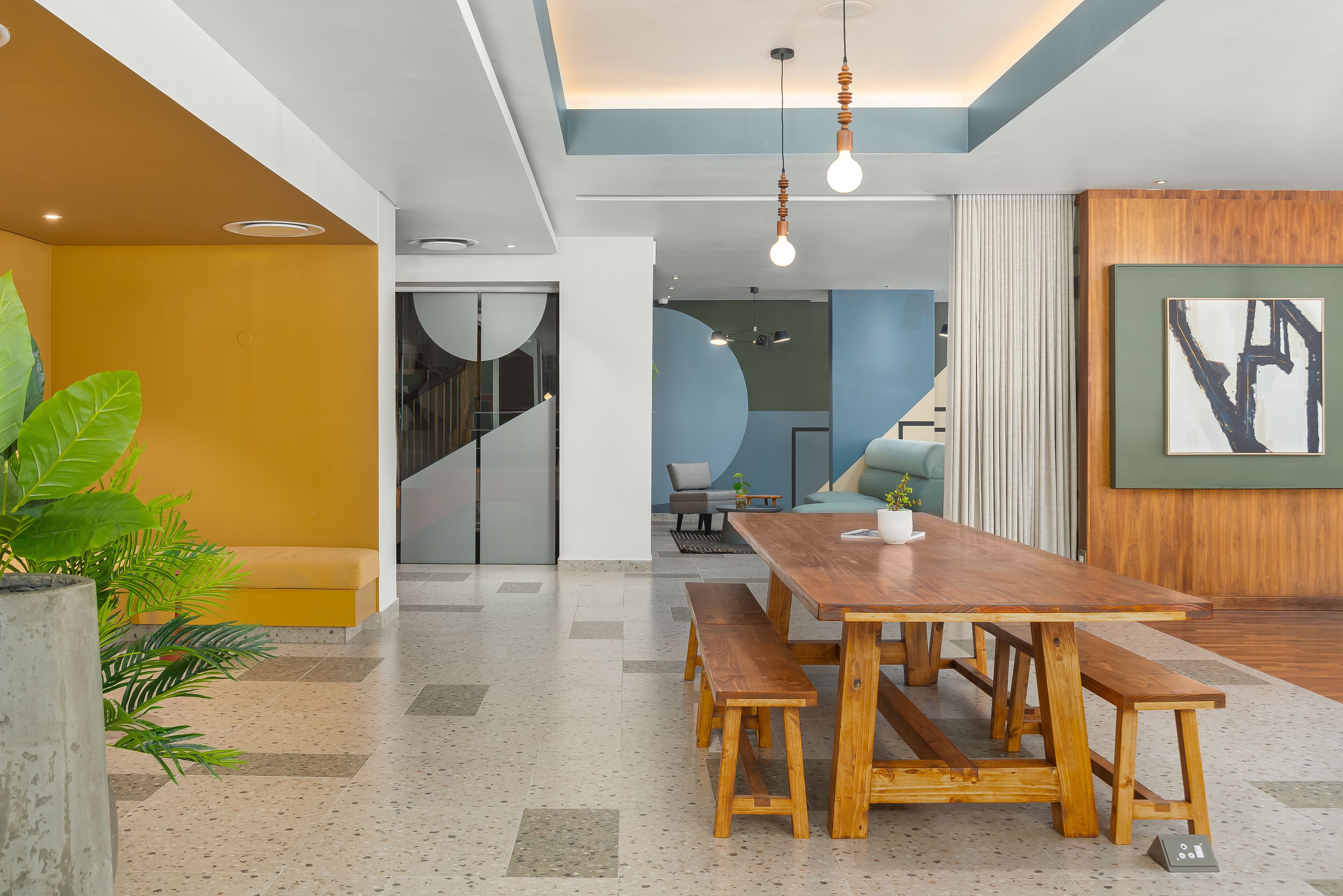 A modern interior with a wooden dining table and benches, a staircase, and a large abstract painting on the wall.