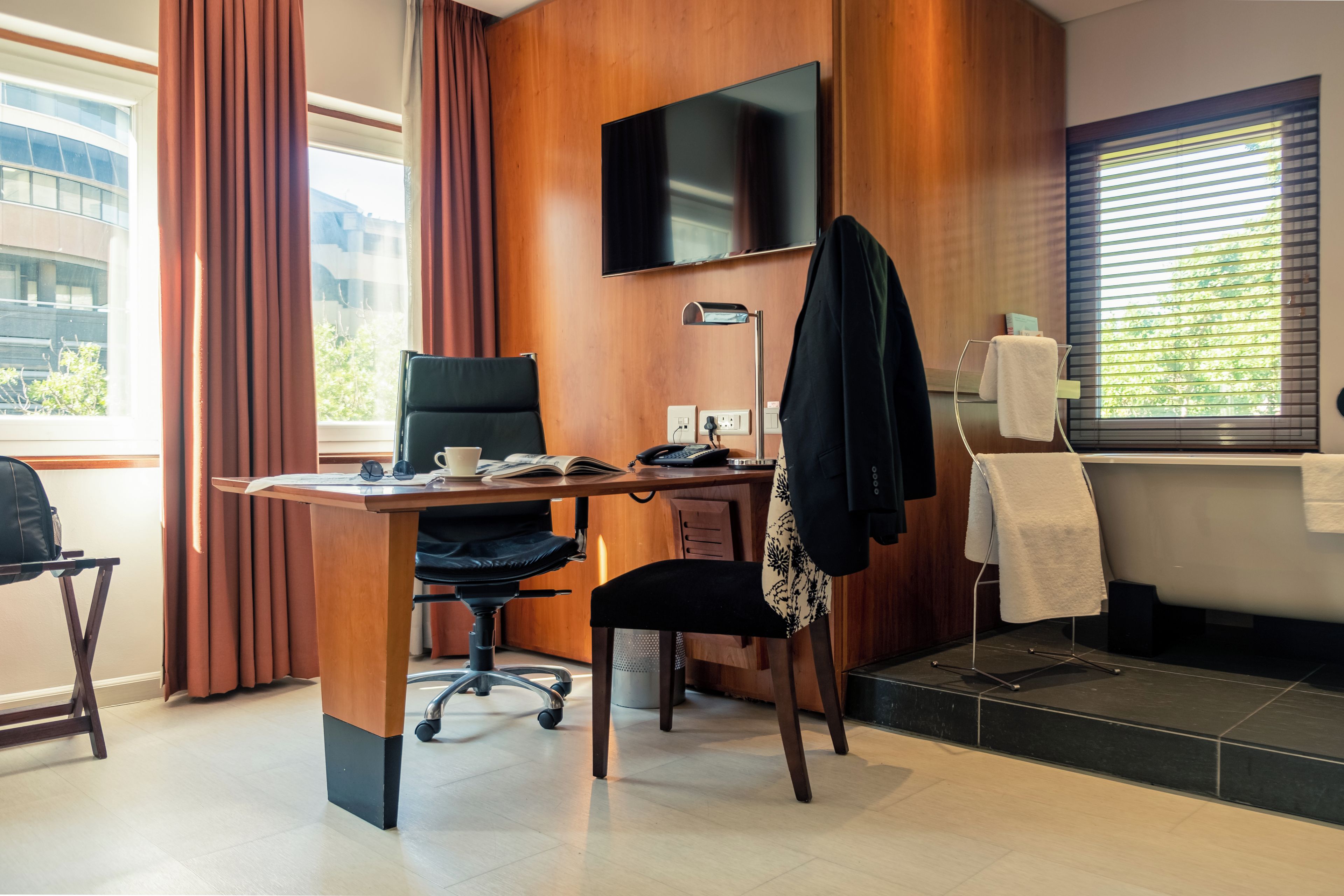 A hotel room with a desk, chair, television, and a view of the outside.