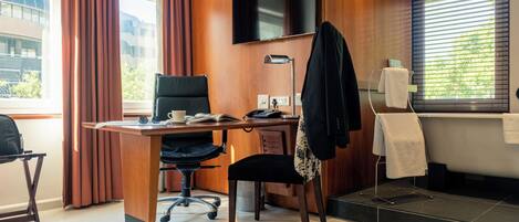 A hotel room with a desk, chair, television, and a view of the outside.