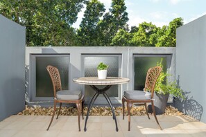 An outdoor seating area with a round table and two chairs, surrounded by a low wall and a potted plant. - Neighbourgood East City (Cape Town)