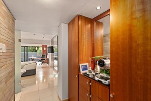 A modern hotel room with a wooden wardrobe, a dining area with a table and chairs, and a view of the outdoors. - Neighbourgood East City (Cape Town)