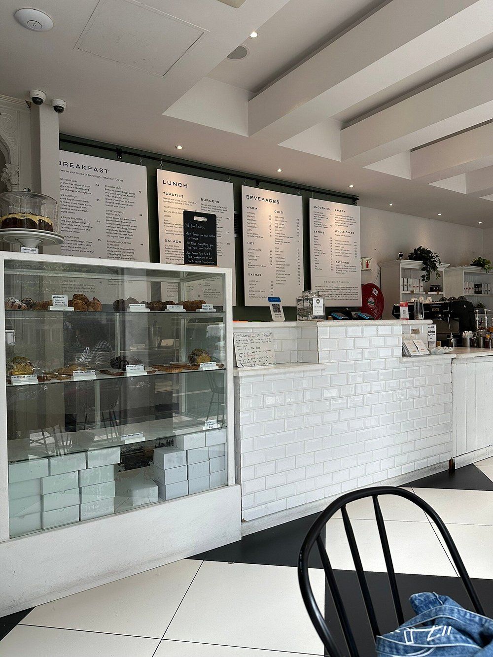 Un interior de cafetería moderna con una pizarra de menú, una vitrina con pasteles y una silla negra.