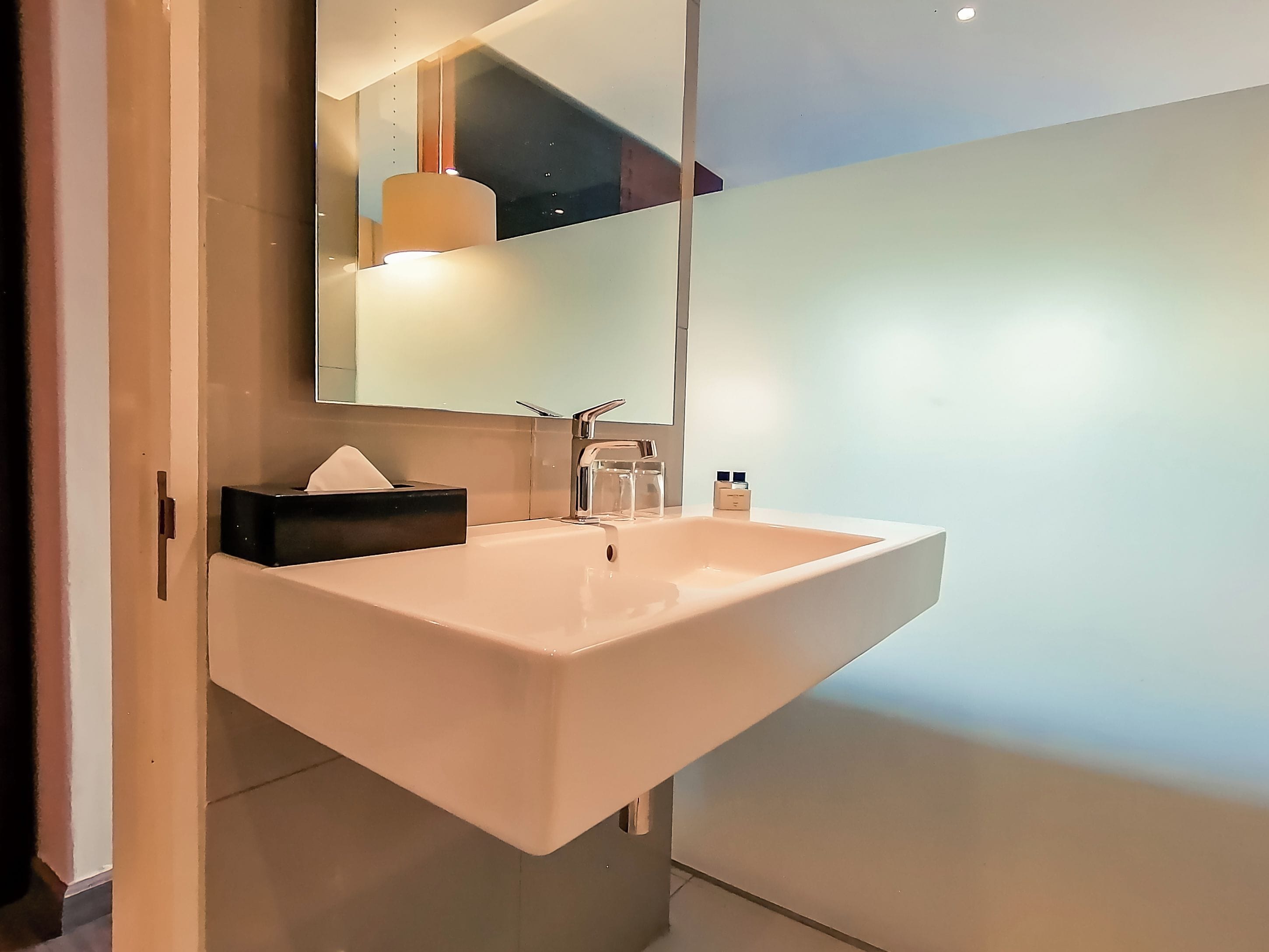 A modern bathroom with a white sink, a mirror, and a towel dispenser.