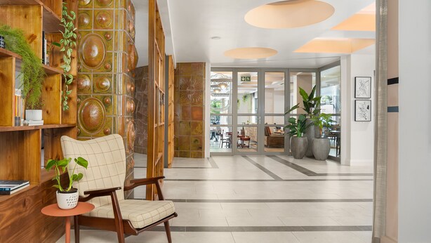 Un vestíbulo moderno con un mostrador de recepción de madera, un sillón acolchado y una planta en maceta.