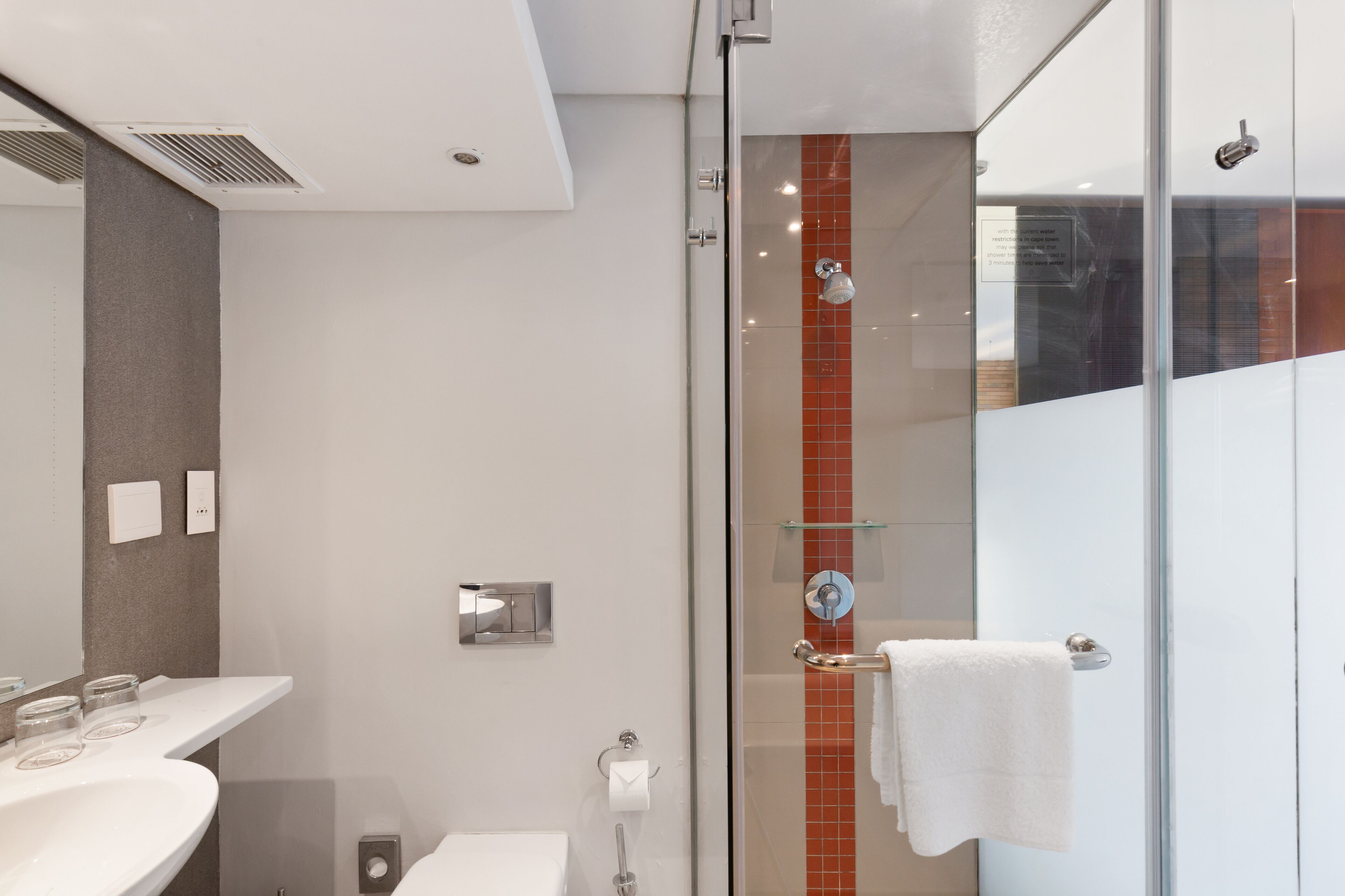Un baño moderno con cabina de ducha de vidrio, un lavamanos blanco y un espejo.