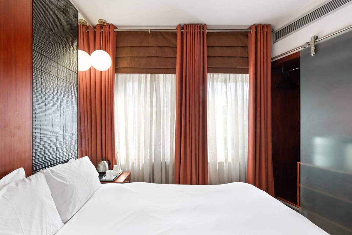 Una habitación de hotel con una cama grande, un armario de madera y una ventana con cortinas.
