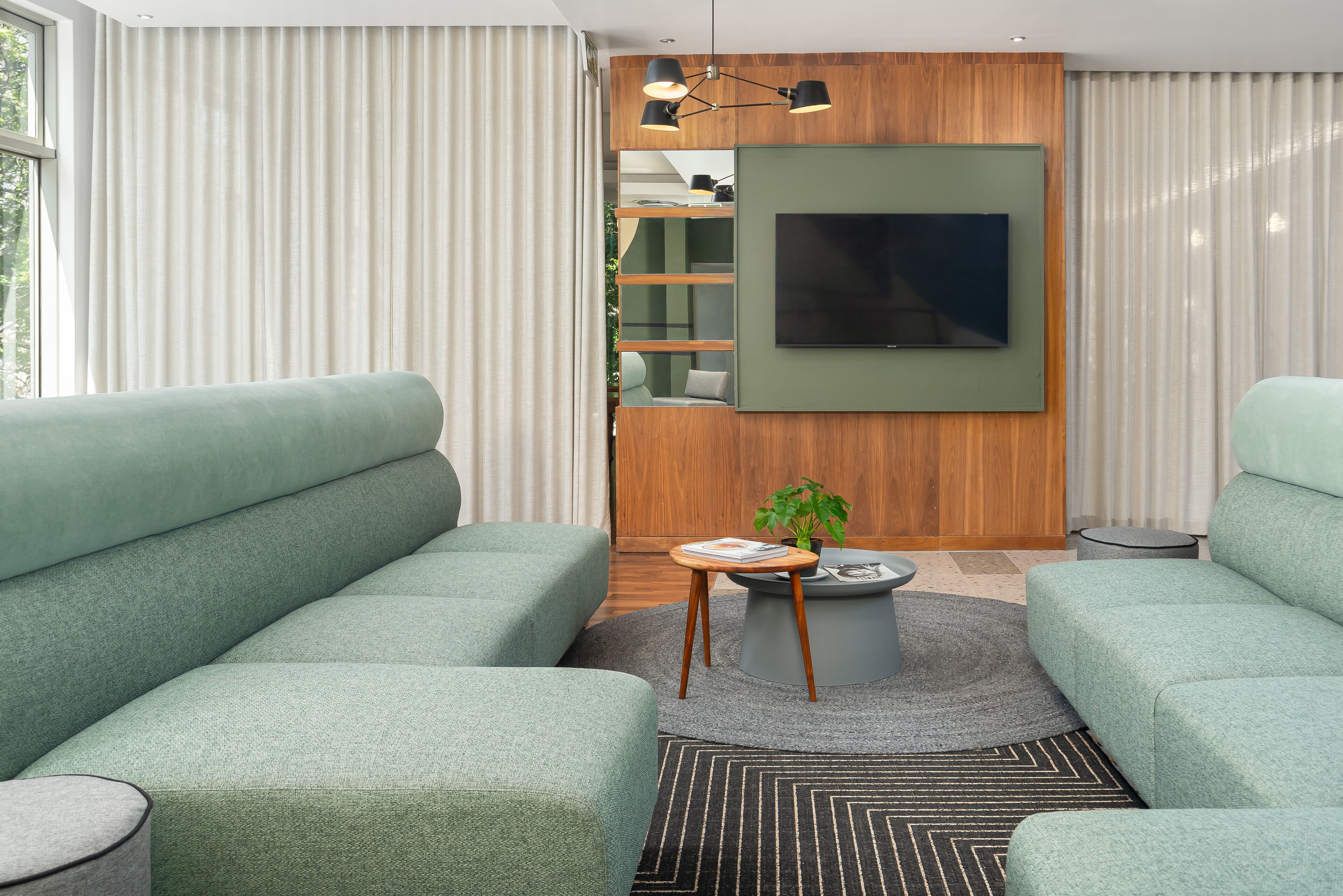 A modern living room with green sofas, a flat-screen TV mounted on a wooden wall, and a small wooden side table with a plant.