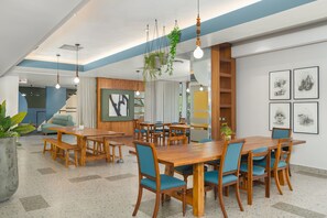A spacious dining area with wooden tables and blue chairs, a large potted plant, and a staircase leading to another level. - Neighbourgood East City (Cape Town)