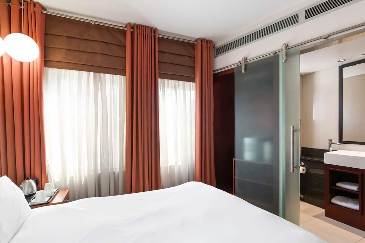 Una habitación de hotel con cama, baño con espejo y cortinas.