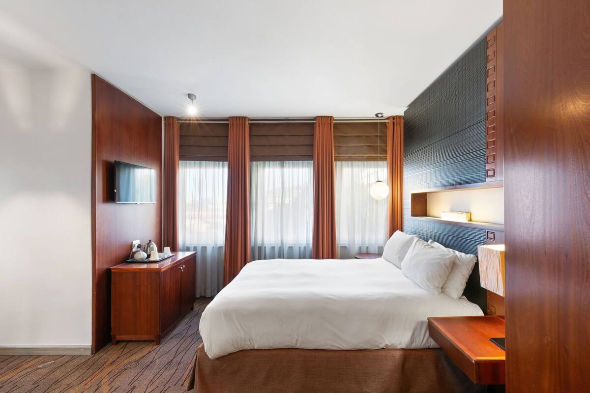 Habitación de hotel con una cama grande, un escritorio, un televisor de pantalla plana y una ventana con cortinas.