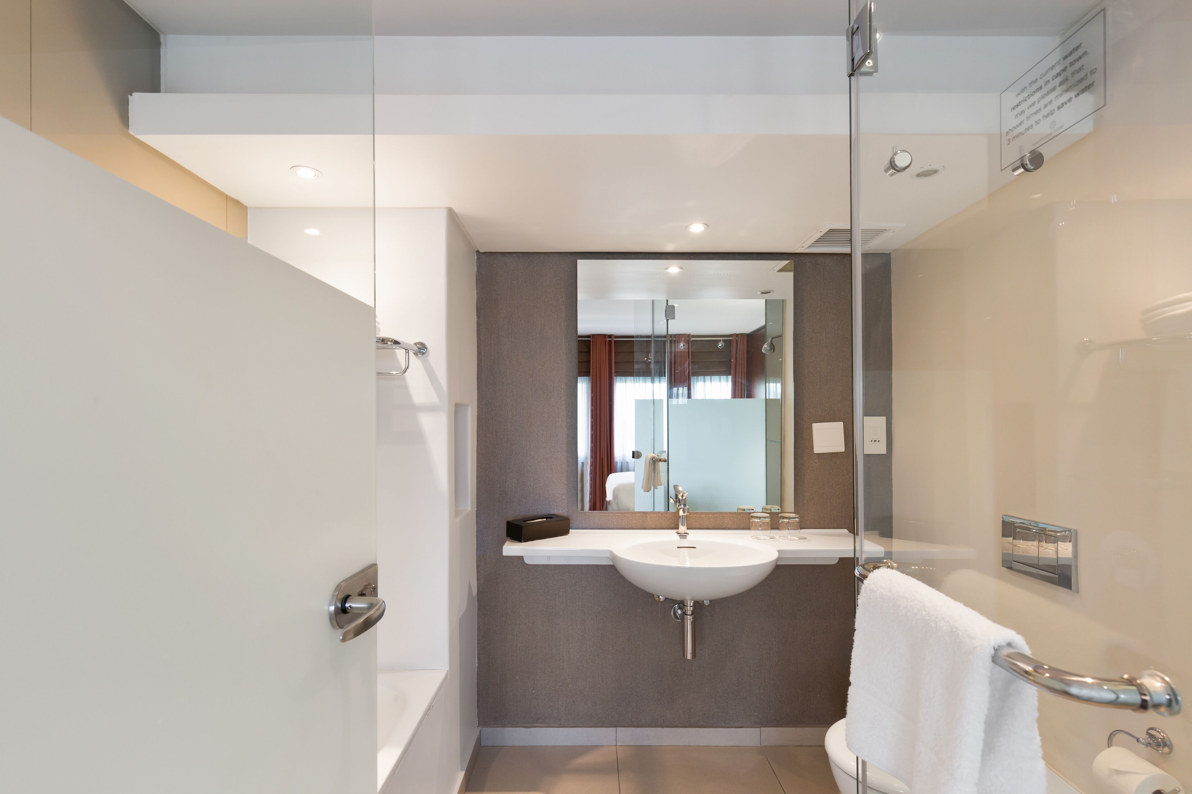 A modern bathroom with a glass shower enclosure, a white sink, and a glass partition.