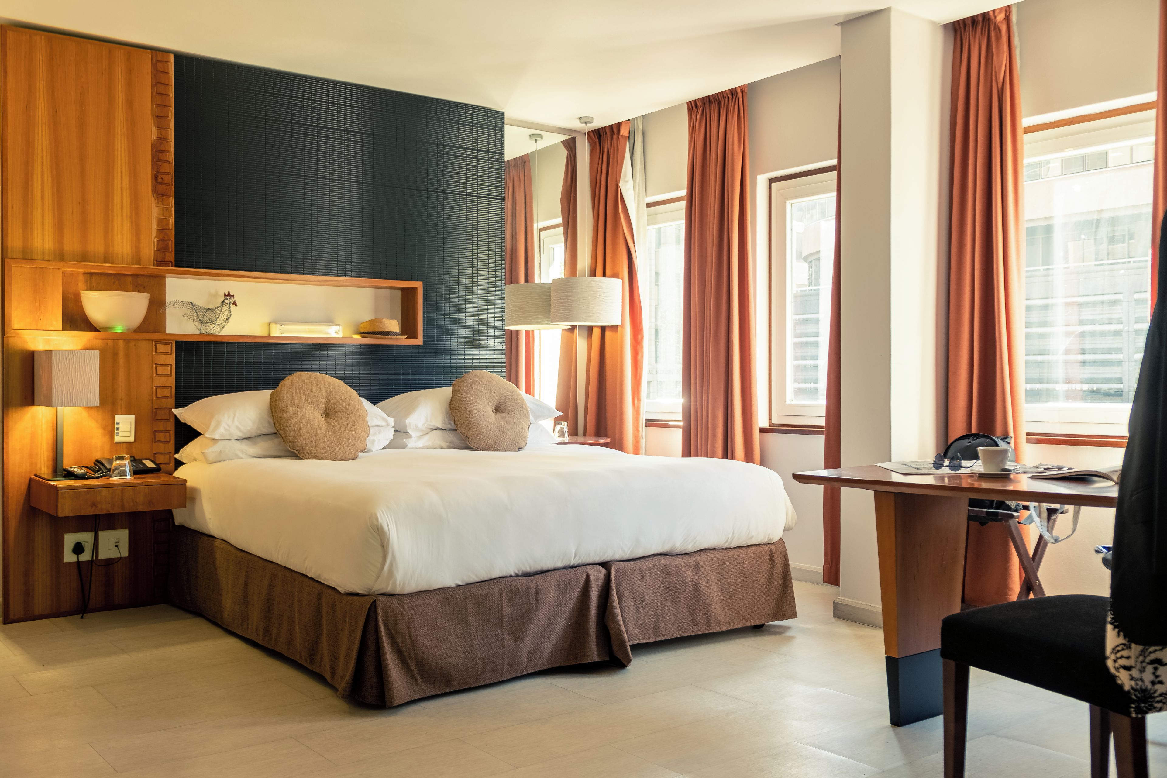A hotel room with a large bed, bedside tables, a desk, and a window with curtains.