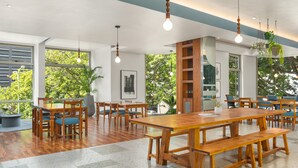 Un comedor amplio con mesas y bancos de madera, ventanas grandes con luz natural y plantas colgantes.